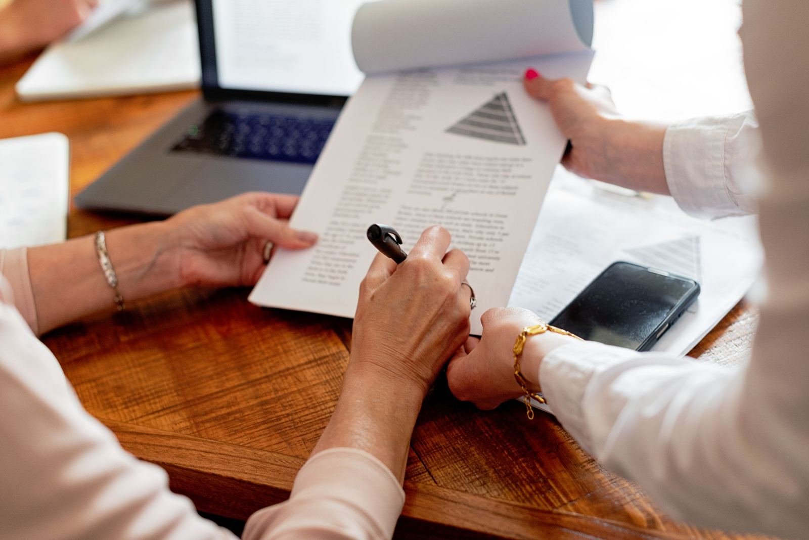 Two people look over a printed program plan that has a pyramid diagram. They sit at a wooden table.