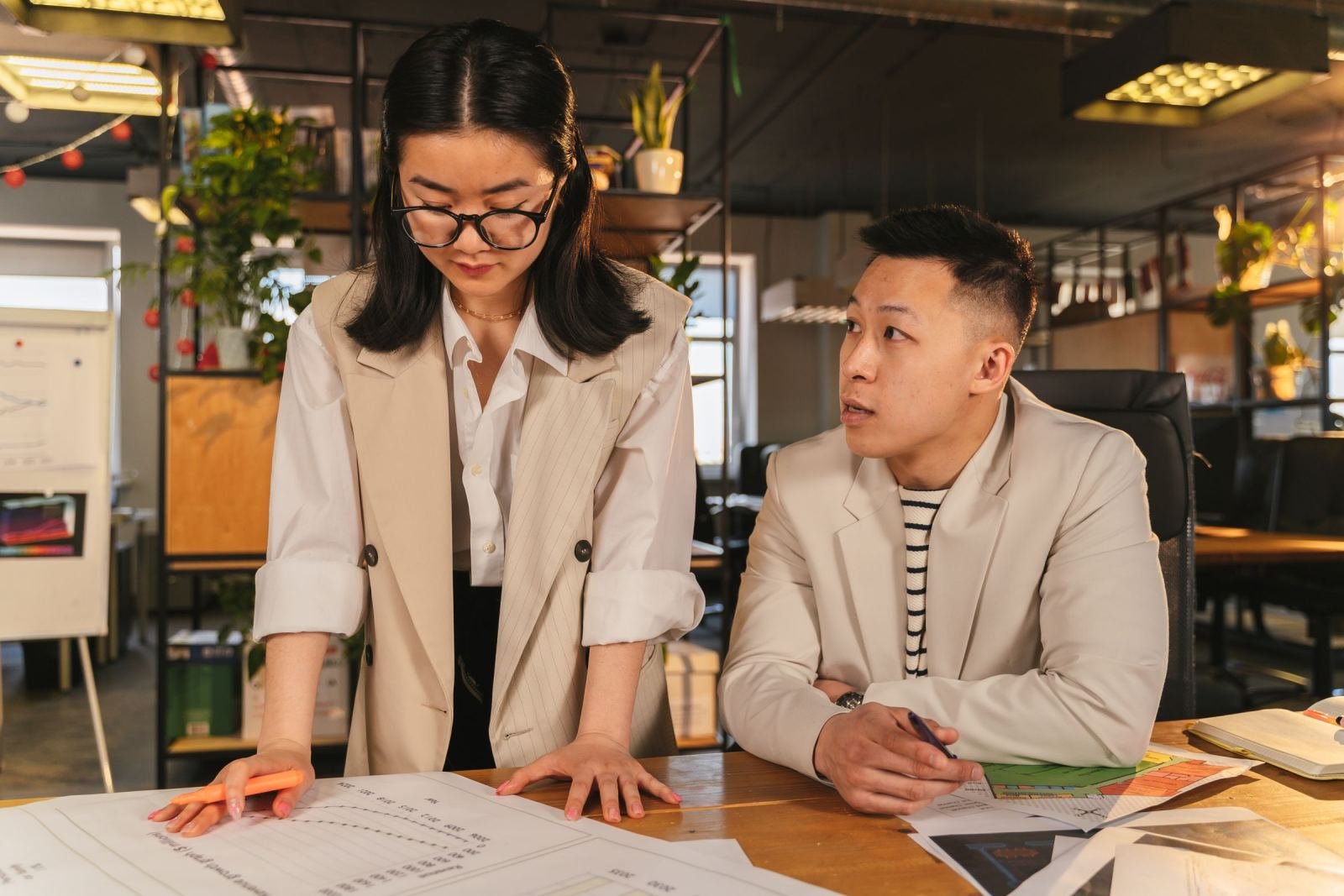 Two colleagues review a calendar and documents at a shared office desk