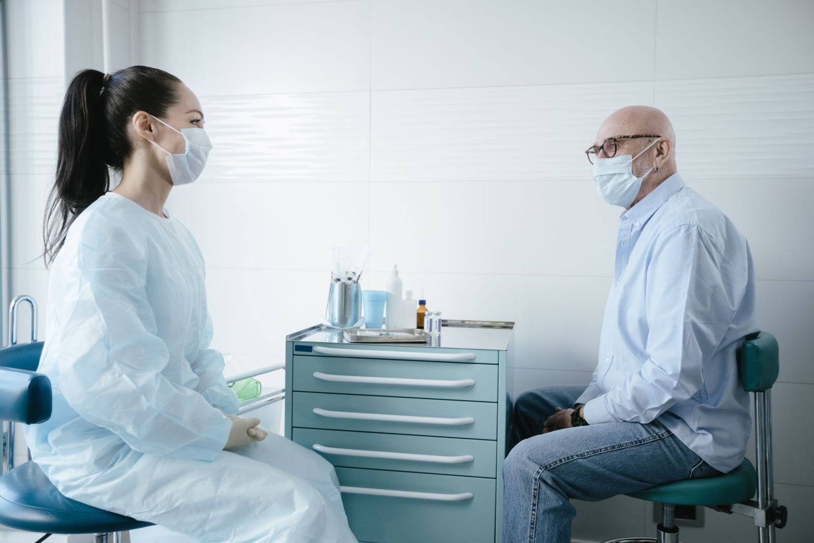 A medical professional and a patient wearing face masks sit facing each other in a bright clinic