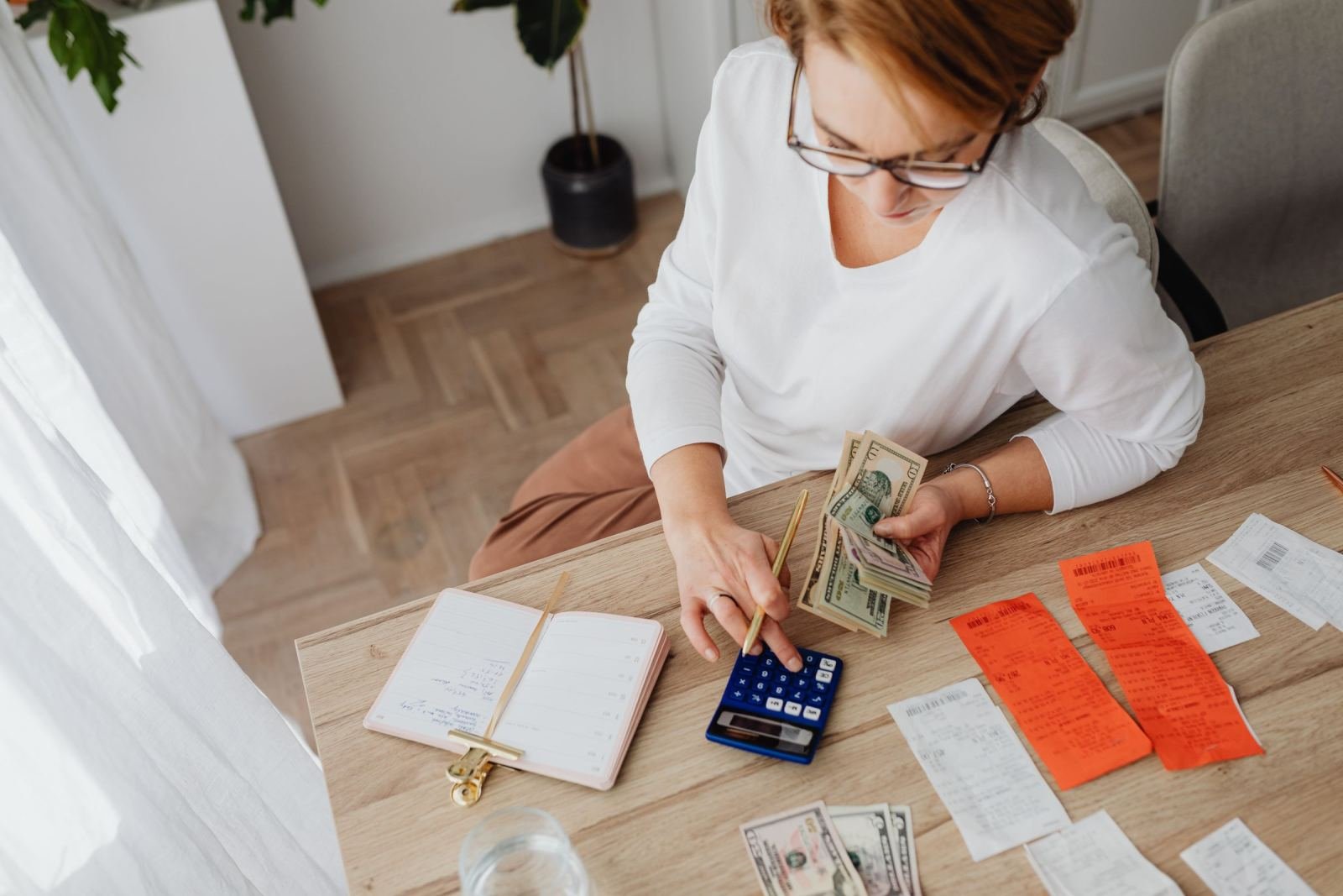 A woman uses a calculator and notebook to manage cash and receipts at a table