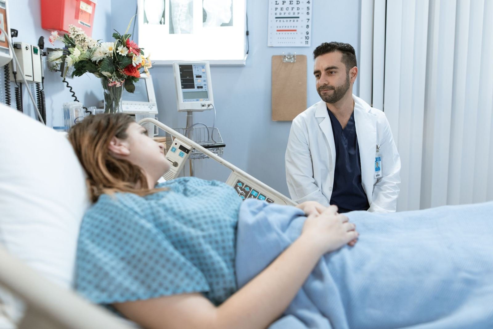 A doctor in a white coat talks with a patient lying in a hospital bed