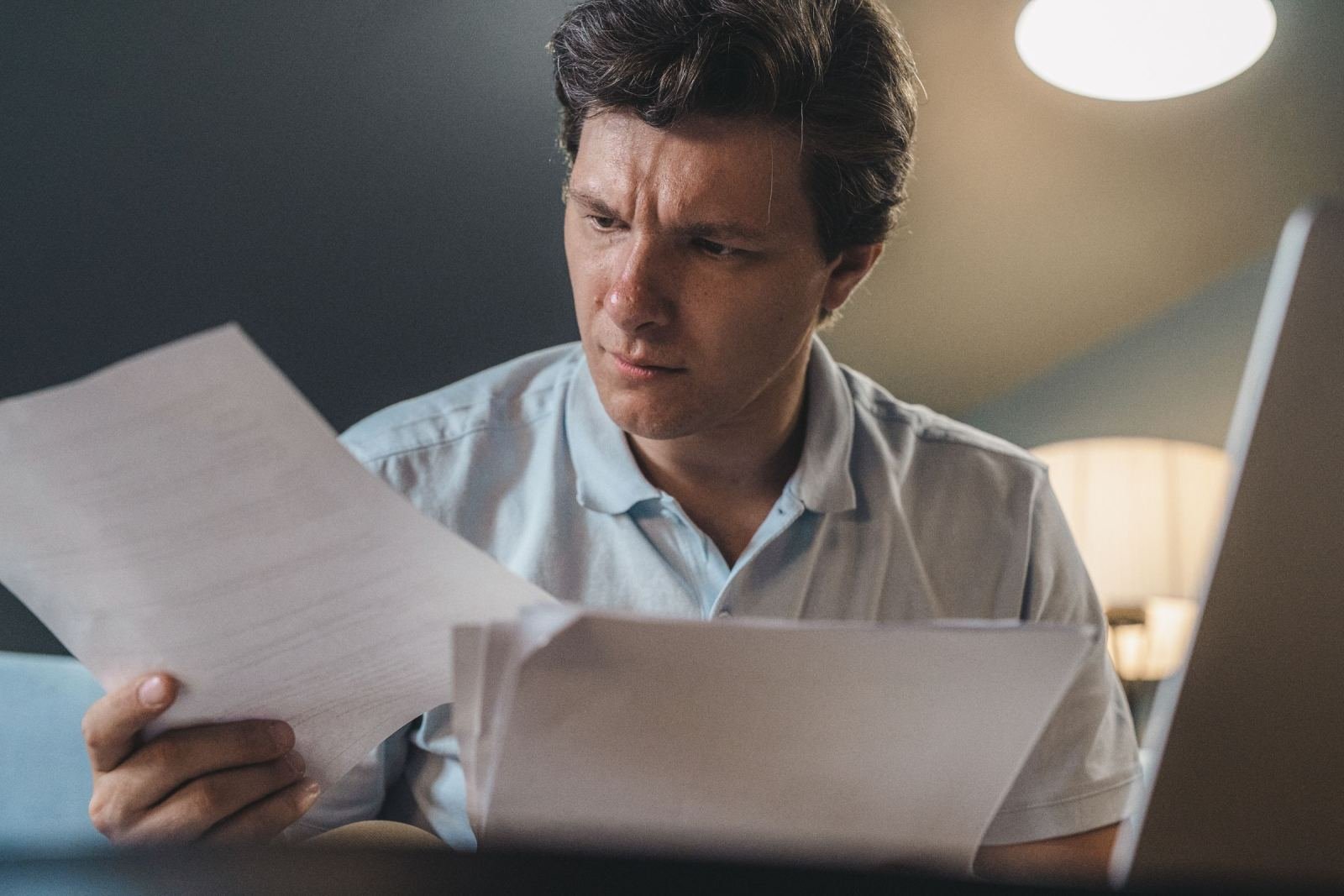 A man with a serious look reads papers on a screen.