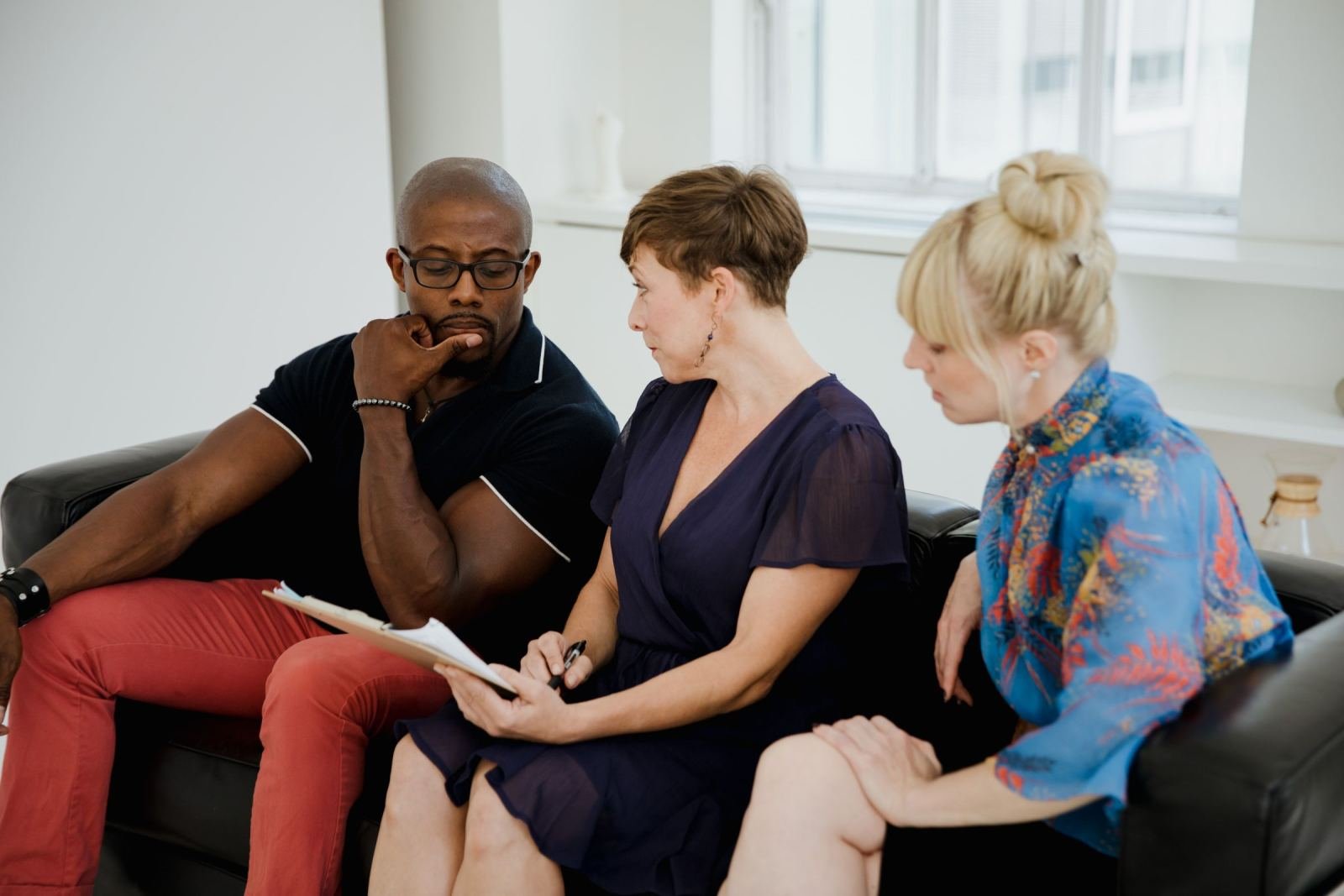 Three people sit on a black sofa while one woman writes on a notepad