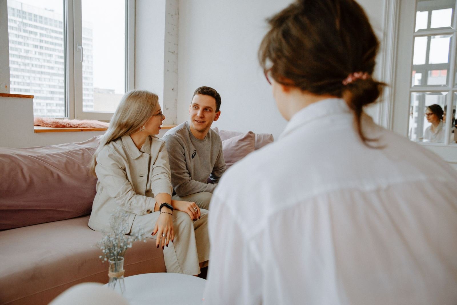 A man and woman sit on a sofa talking to a counselor seen from behind