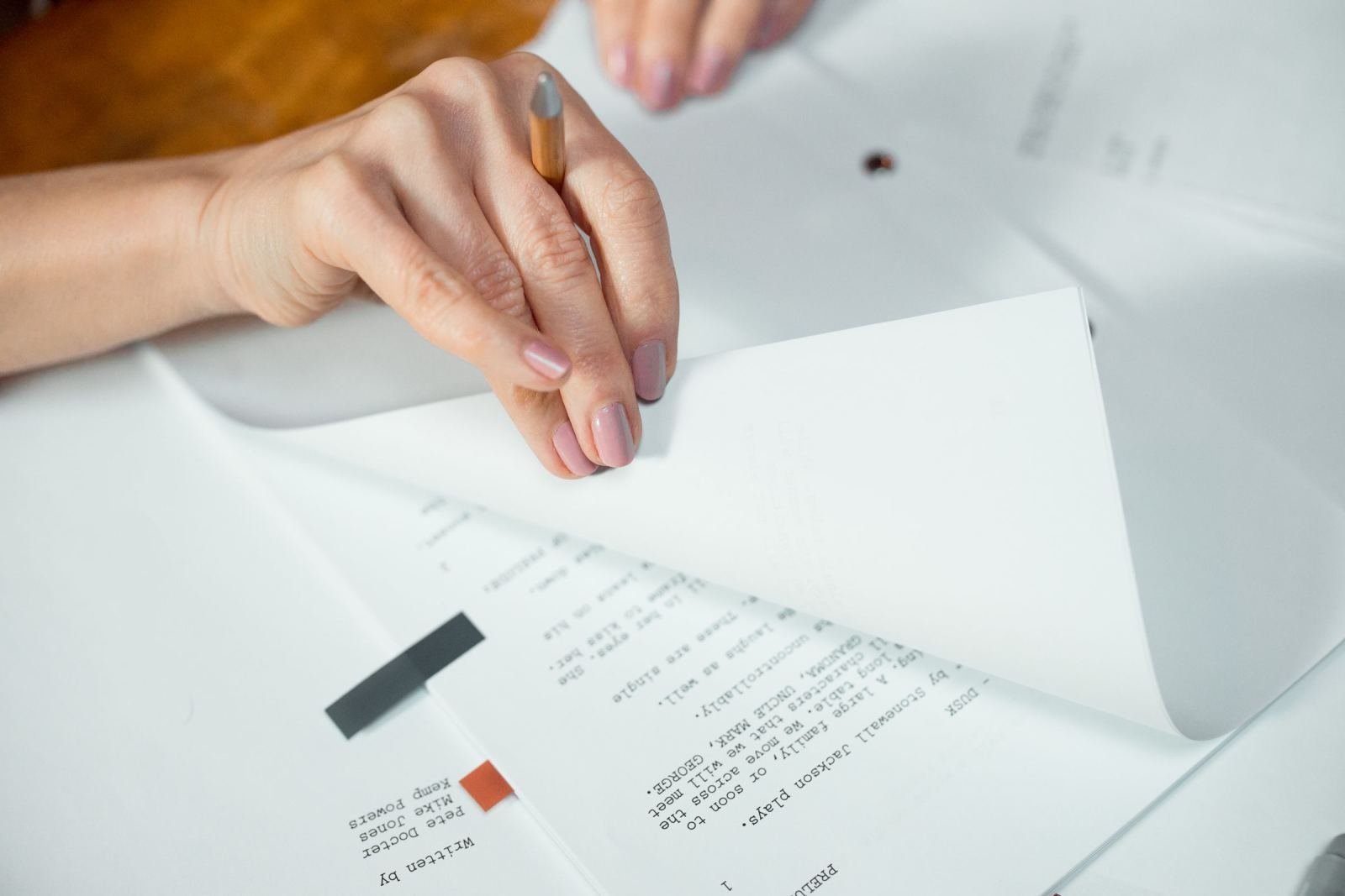 A person's hands lifting a white page to read printed text on a desk