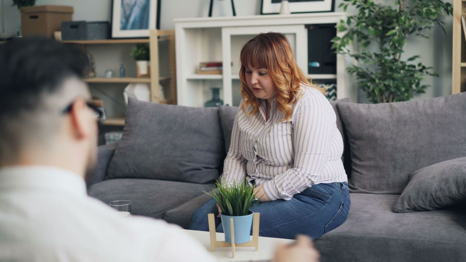 A woman sits on a gray sofa talking with a man in a bright office