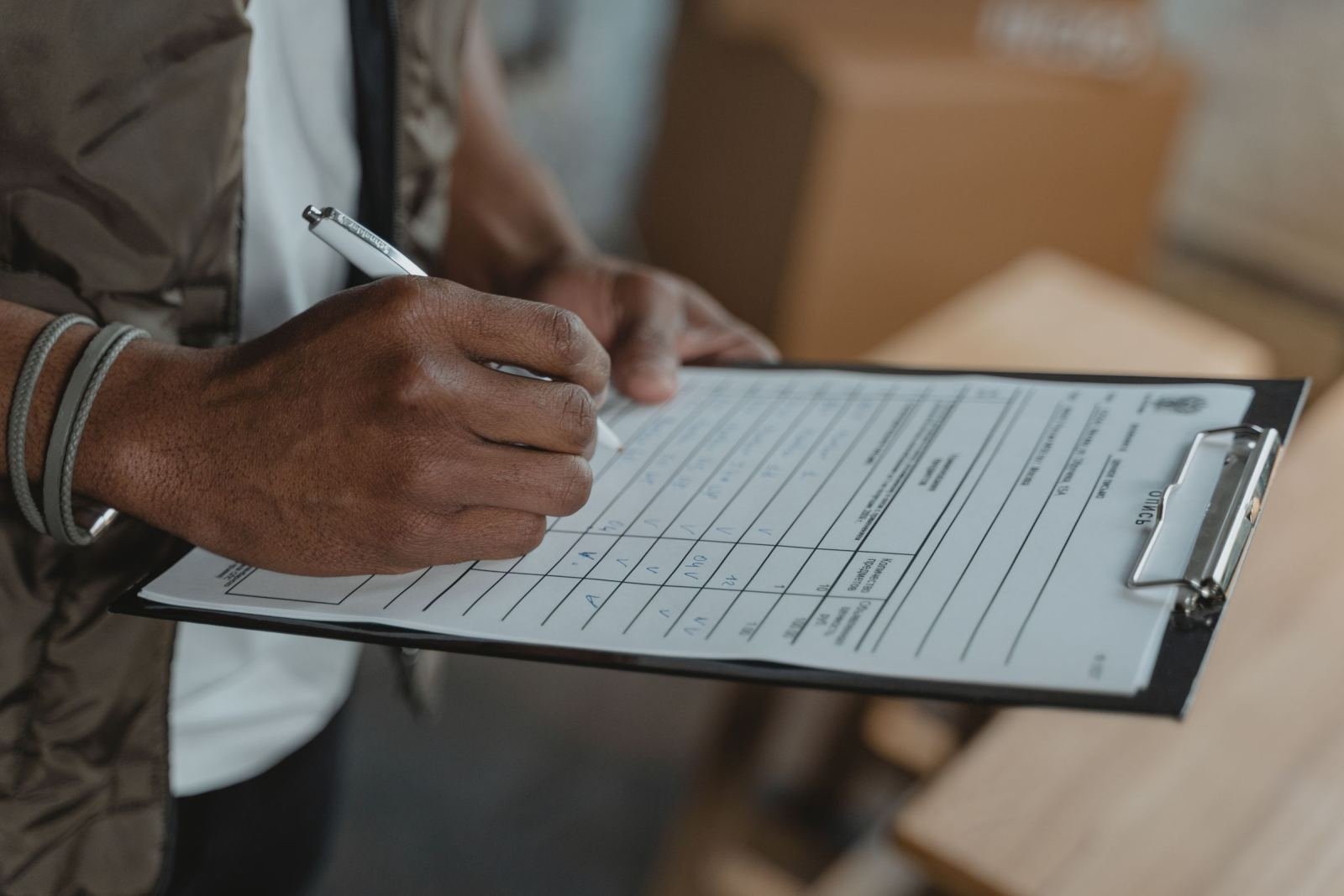 A person's hands writing on a checklist on a clipboard