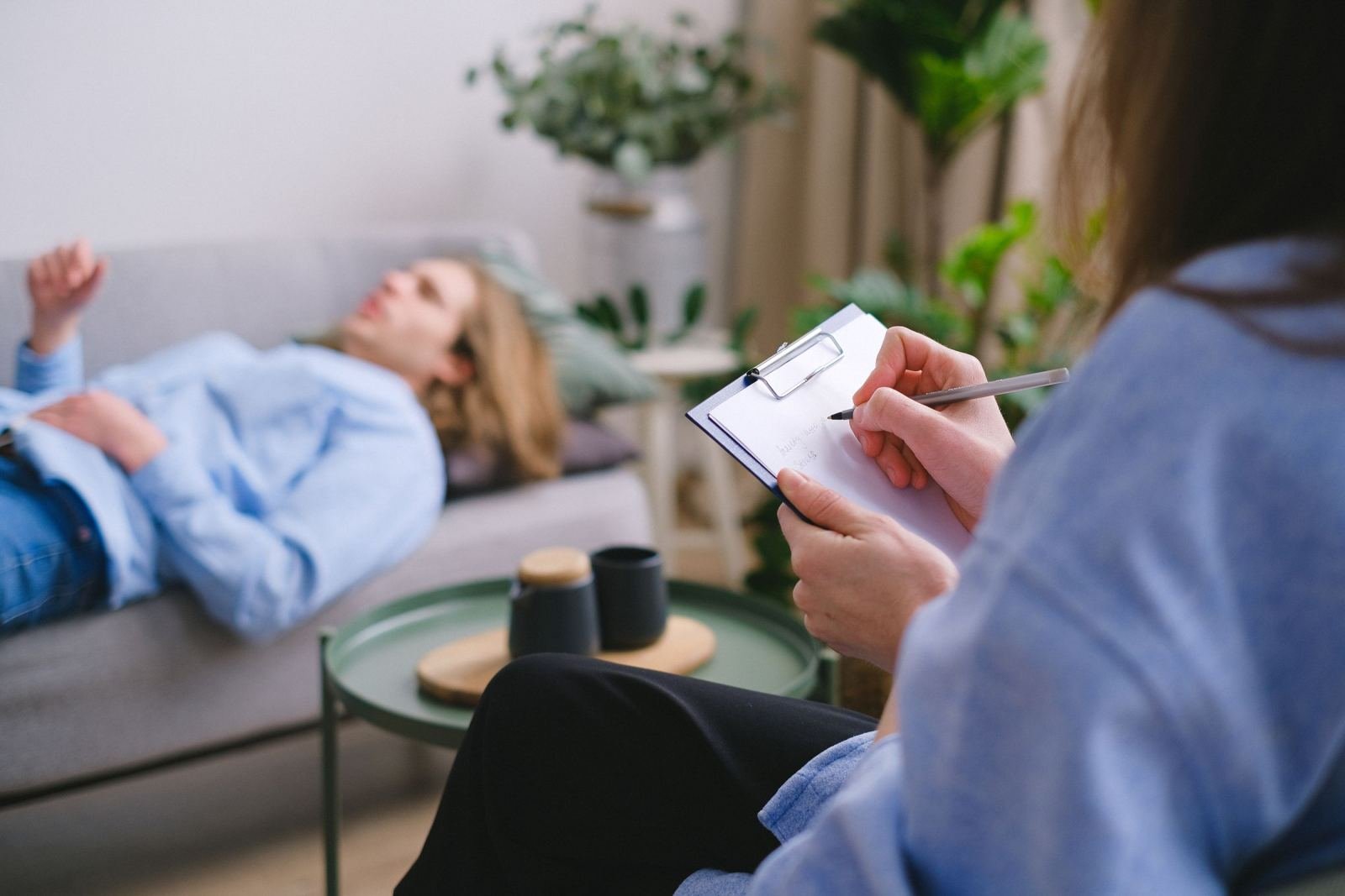 A woman relaxes on a couch while a specialist writes on a clipboard.