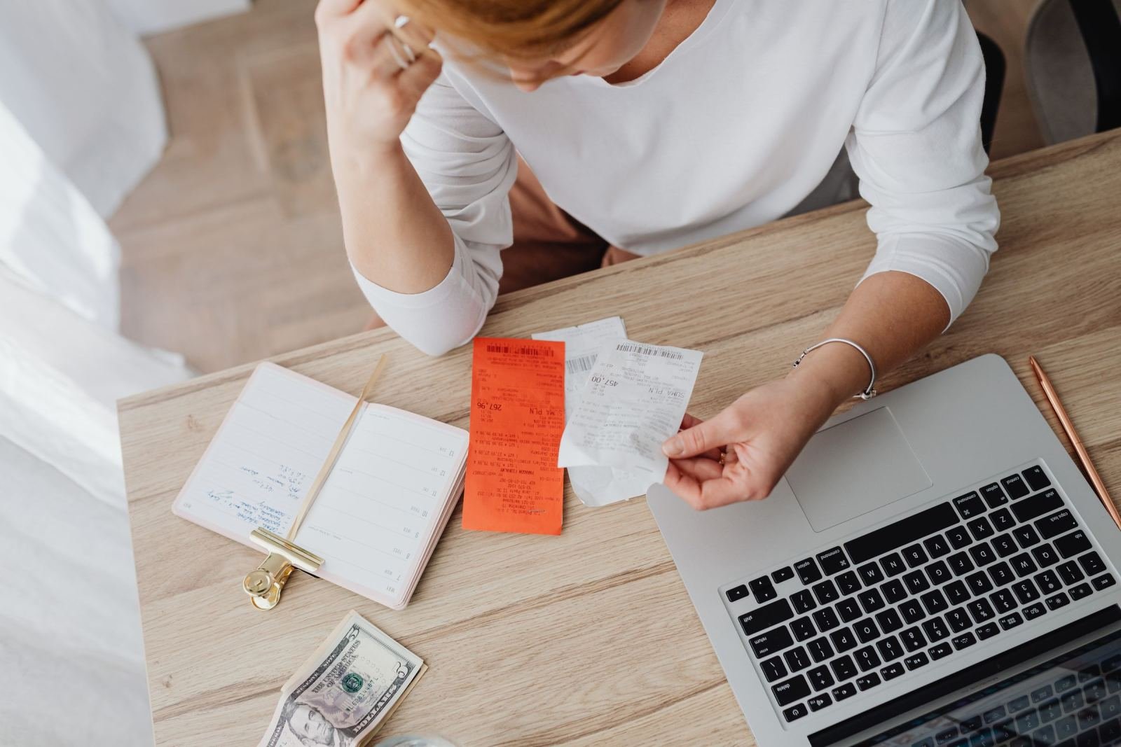 A person at a desk with a laptop, notebook, and paper receipts