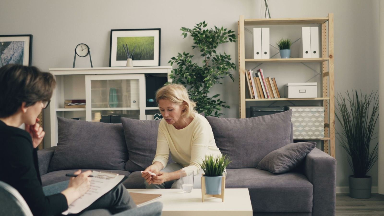 A woman speaks with a professional holding a clipboard in a calm office setting