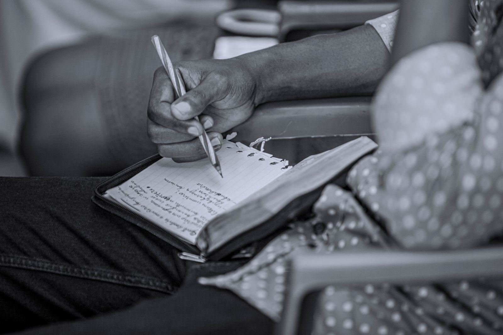 A person writing notes in a small notebook with a pen