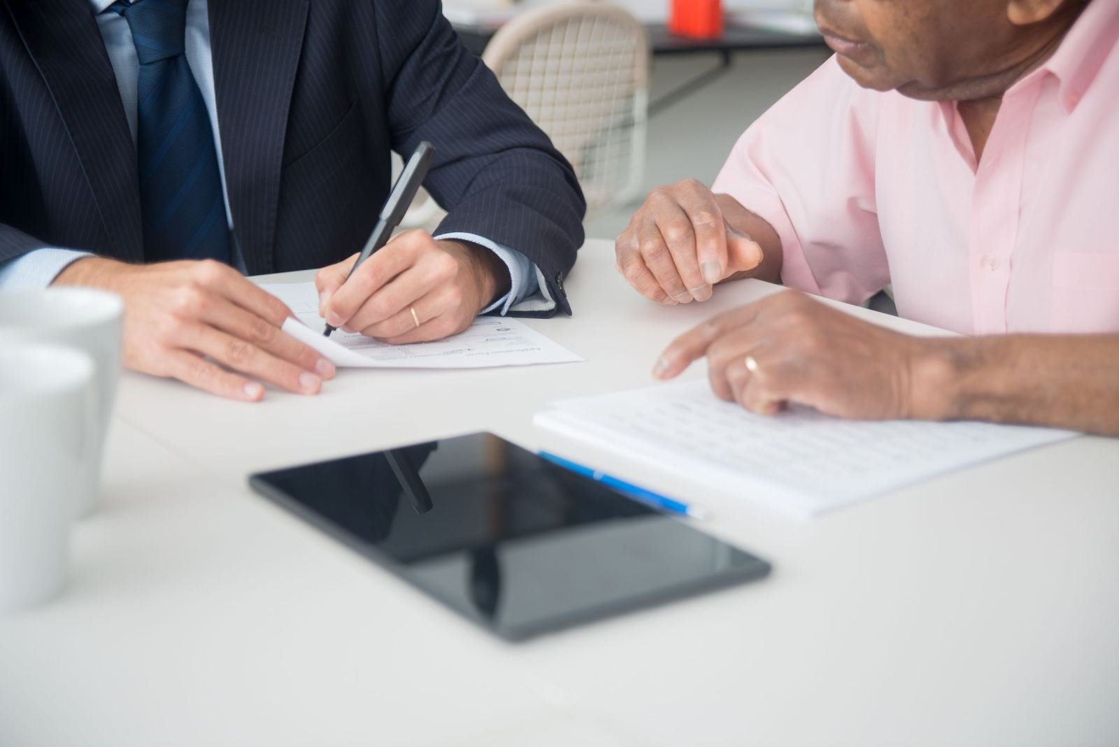 Two people review documents together at a white table with a tablet