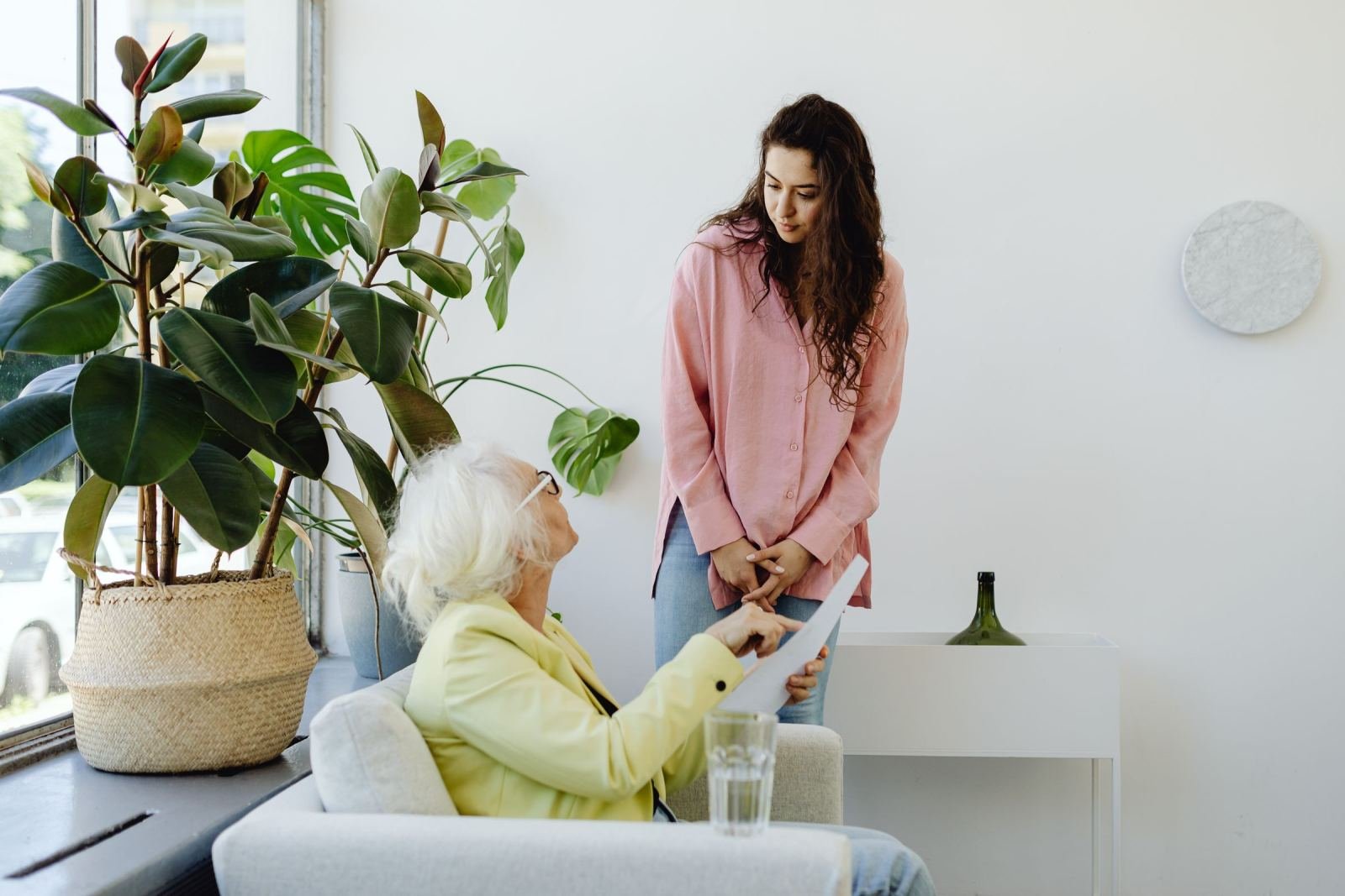 A woman in a pink shirt talks with an older woman holding a piece of paper